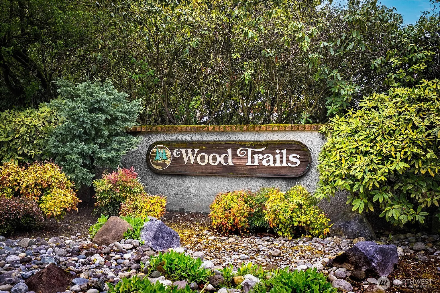 The Wood Trails entrance sign, set in river rock and flanked by rhododendrons